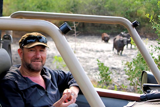 Kobus Carstens in a game drive vehicle with buffalo in a river in the background.