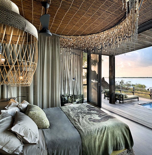 A safari bedroom opening onto a wooden deck with a couple sitting in a private pool facing the Zambezi River in Zambia.