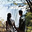 A couple holding hands while standing at a viewpoint overlooking Victoria Falls.