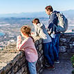 A father and two children at a mountain viewpoint looking out over a coastal city.