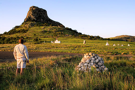A guide standing in a grassy field looking toward the historical battlefields and Isandlwana hill.