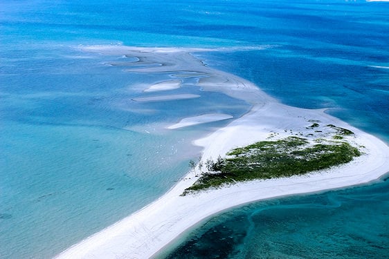 Aerial view of a white sandbar and tropical island surrounded by clear ocean waters.