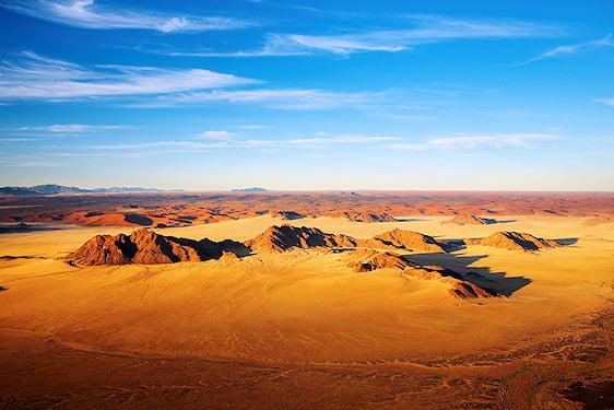 Aerial view of sand dunes and mountain ridges in the Namib Desert.