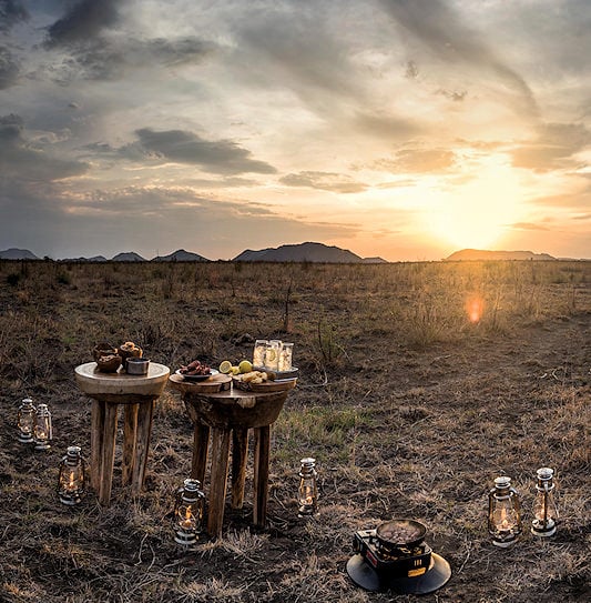 A safari picnic setup with tables and lanterns in the open veld at sunset, Madikwe Game Reserve.