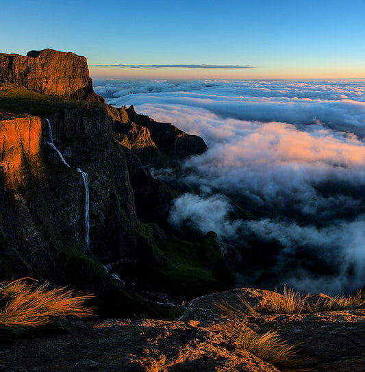 Tugela Falls flowing down a cliff face above clouds at sunrise, Drakensberg.