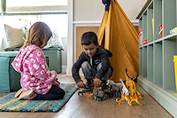Two children playing on a rug with toy animals in front of a toy teepee.
