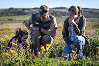 A guide, a woman, and a child kneeling in a field of yellow wildflowers.