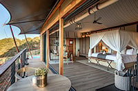 A luxury safari tented bedroom opening onto a wooden deck.