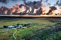 An aerial view of a safari lodge surrounded by grassy plains under a sunset sky at Shamwari Private Game Reserve.