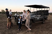 A family standing next to an open safari vehicle during a stop in the bush.