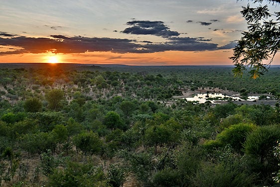 A sunset view overlooking a wooded landscape and a small waterhole in the Victoria Falls area.