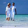 Man and woman wading through clear shallow water on a beach.