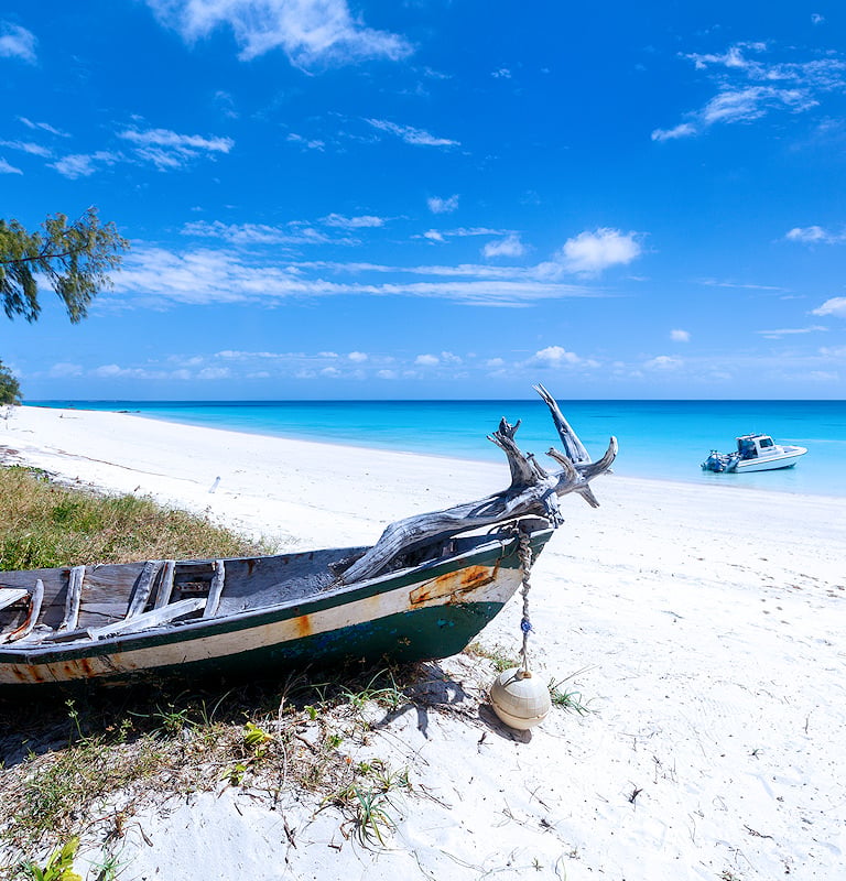 Wooden boat resting on a sandy shore next to clear blue water.