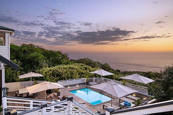 Wooden pool deck with sun loungers overlooking coastal forest and ocean on South Africa's Wild Coast.