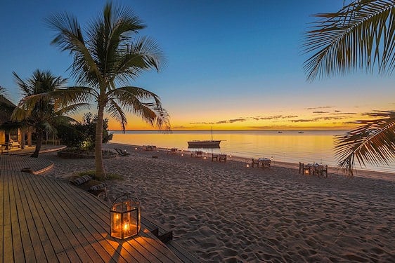 Outdoor dining tables and lantern light on a palm-lined beach at evening in the Bazaruto Archipelago.