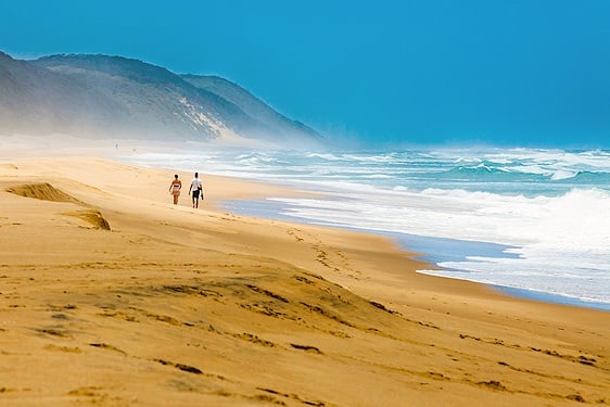 Couple walking along a sandy KwaZulu-Natal beach bordered by high coastal dunes