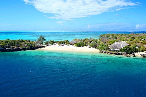 Aerial view of a sandy cove and thatched lodge surrounded by ocean in the Quirimbas Archipelago.