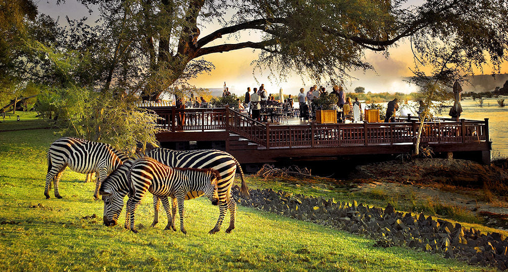 Tourists on a deck at the Royal Livingstone Hotel with the Victoria Falls behind them.