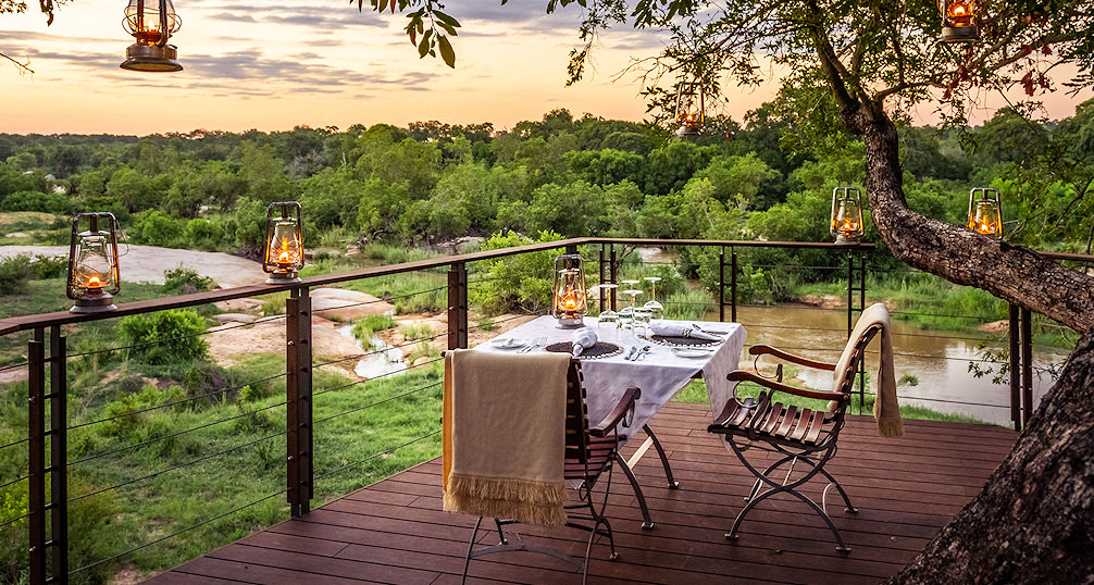 An elegant dining deck at Dulini against a orange sunset.