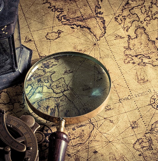 A magnifying glass, a lantern, and a brass navigation tool on a world map.