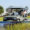 An open 4x4 safari vehicle driving through shallow water.