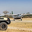 A light aircraft parked on a bush airstrip next to a safari vehicle.