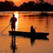 A poler standing in a traditional wooden canoe navigating calm water.