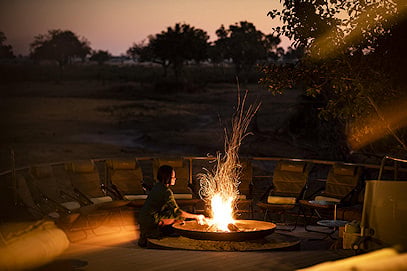 A guest tending to a boma fire pit on an outdoor viewing deck at night.