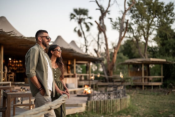 A couple relaxing on the wooden deck of a safari lodge in the Linyanti wilderness.