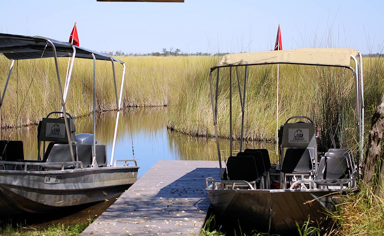 Safari motorboats docked at a wooden pier in the reeds, Botswana.