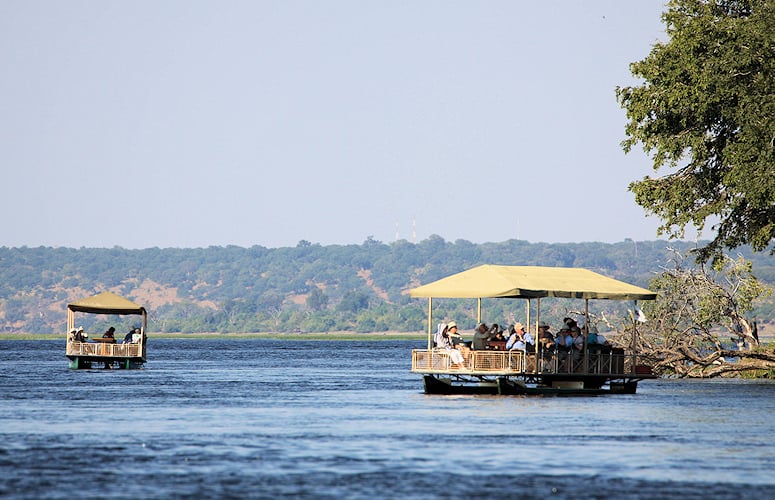 Travelers on covered safari boats cruising on the river, Chobe, Botswana.