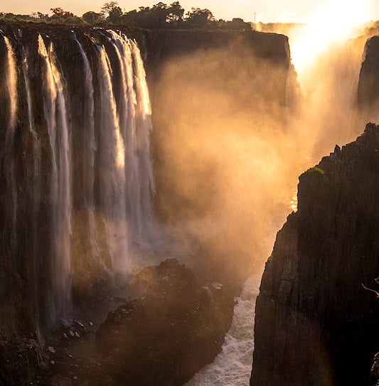 A view through a ravine at Victoria Falls, Zambia, with the spray glowing golden in the sun.