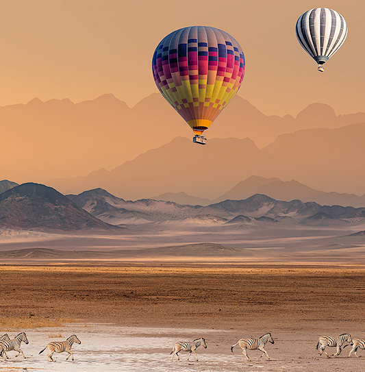 Hot-air balloons drifting in the sky of Namibia while zebras run across the salt pan below.