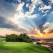 Golden rays breaking through clouds over a putting green beside a river.