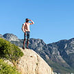 A hiker standing on a high rock outcrop looking out over mountain peaks.