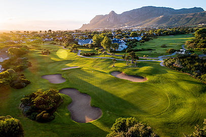 Warm sunlight illuminating a putting green and sand traps at the base of a mountain ridge.