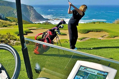 A golfer at the top of her swing on a seaside tee box overlooking coastal cliffs.