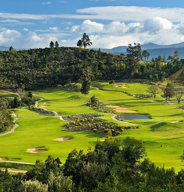 Rolling green fairways and bunkers winding through countryside hills with distant mountains.