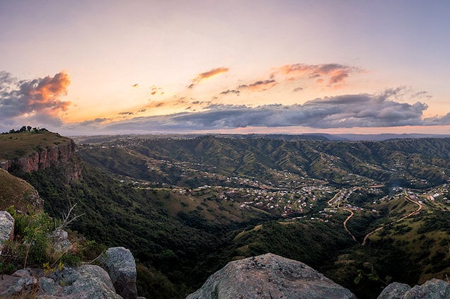 Wide view across a deep valley with rural settlements from a rocky cliff edge at dusk.