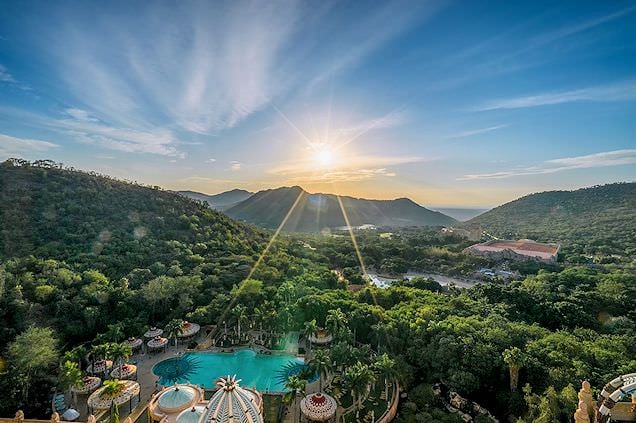 High aerial view of the Sun City resort pool set in a valley surrounded by forested hills.