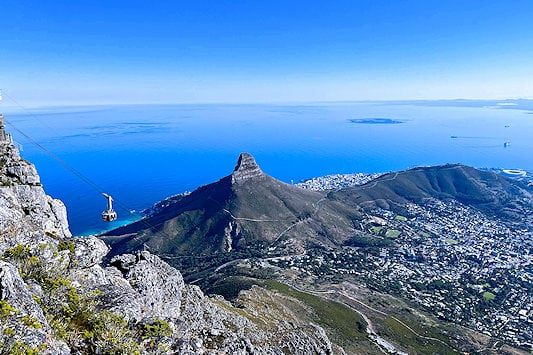 Table Mountain aerial cableway car descending with Lion's Head and the Atlantic coastline in the background, Cape Town.