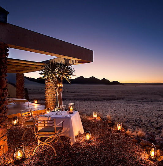 A private luxury dinner table set with lanterns overlooking the desert plains of Sossusvlei in Namibia.