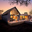 A modern safari villa warmly lit at dusk with candles along the outdoor walkway.