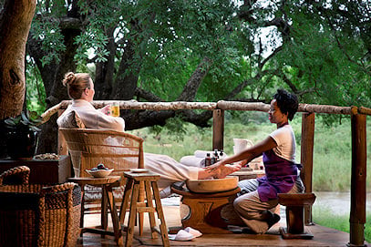 A guest receiving a foot massage on a private balcony overlooking a river.