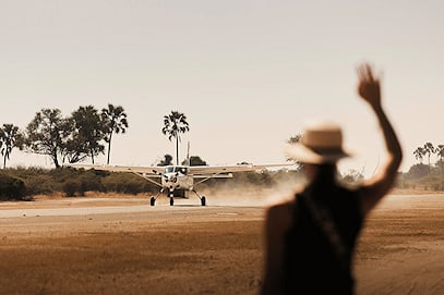 A light aircraft landing on a dirt bush airstrip.