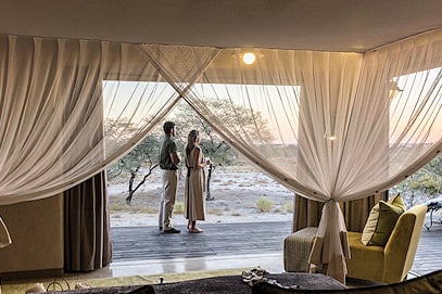 A couple standing in an open suite entryway looking out over grasslands.