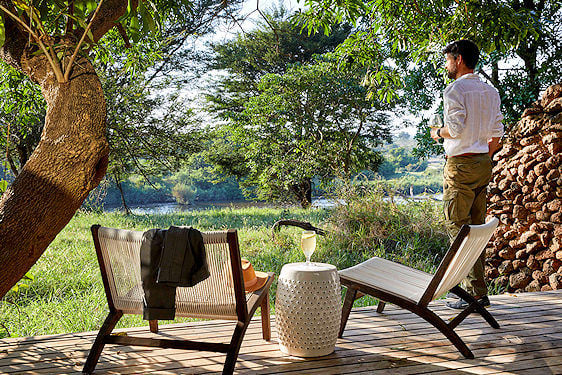 A guest standing on a viewing platform with a drink, looking out over a riverbank in Sabi Sand.
