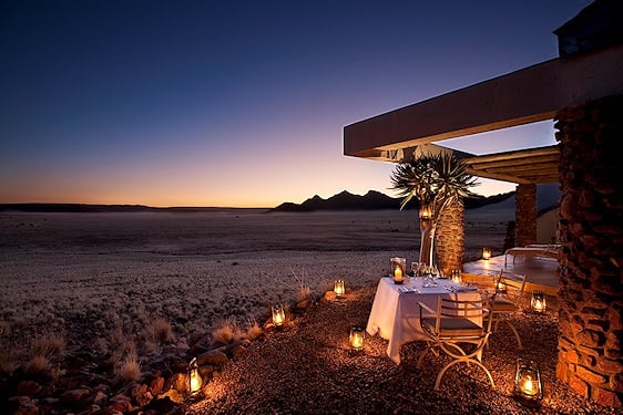 A lantern-lit private dinner table set on a gravel terrace facing the desert plains of Sossusvlei.