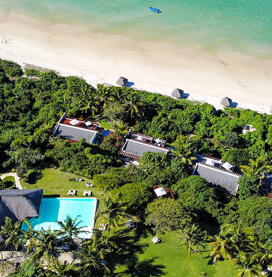 Aerial view of coastal hotel buildings and a swimming pool along a sandy shoreline in Vilanculos, Mozambique.