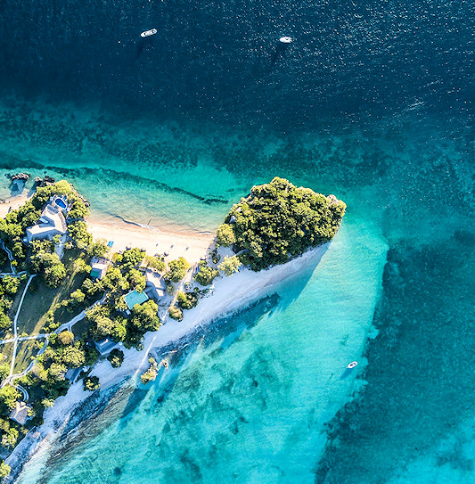 An aerial view of a beach lodge built among trees on a coastal headland in the Quirimbas Archipelago, surrounded by clear turquoise water.